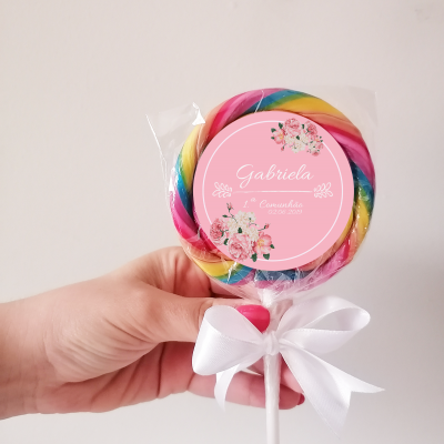 Pirulito colorido com etiqueta rosa e laço branco segurado por mão em fundo branco