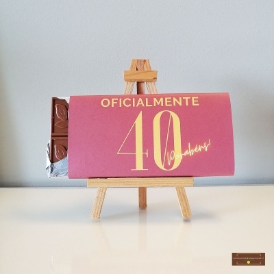 Barra de chocolate com embalagem rosa e texto amarelo sobre um cavalete de madeira