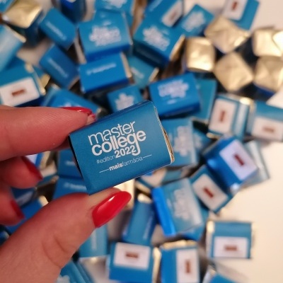 Caixa azul pequena com chocolate 'master college 2022' em mão com unhas vermelhas