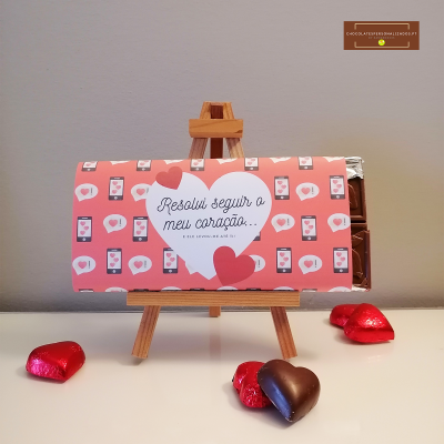 Barra de chocolate em embalagem rosa com corações e texto, em cavalete com bombons de coração vermelhos