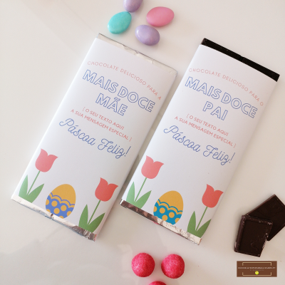 Dois tabletes de chocolate com embalagens temáticas de Páscoa decoradas com tulipas e ovo, rodeados por chocolates coloridos e pedaços de chocolate.