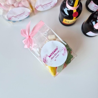 Embalagens de doces coloridos com etiqueta BATIZADO Pink Garden e fita rosa, ao lado de pequenas garrafas de bebida com tampa vermelha