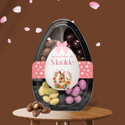 Ovo de plástico transparente com amêndoas de chocolate coloridas e etiqueta decorativa com coelho e texto