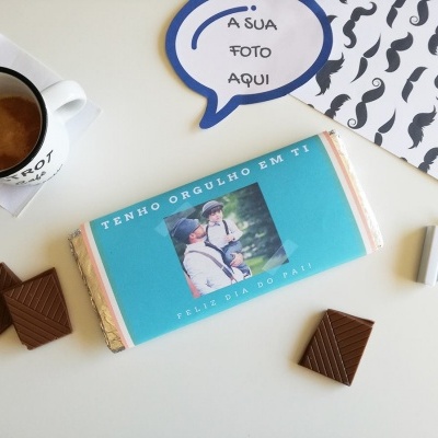 Barra de chocolate personalizada com foto numa superfície branca com pedaços de chocolate, caneta, moldura com bigodes e chávena de café