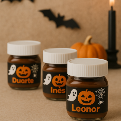 Frascos de vidro pequenos decorados para Halloween com nomes Leonor, Inês e Duarte, com velas, abóboras e morcegos ao fundo.