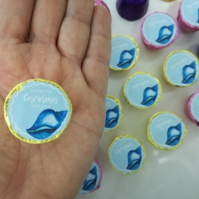 Pirulitos redondos com embalagem azul claro e concha azul, segurado na mão