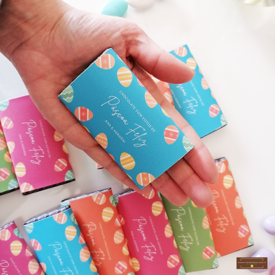 Caixa de chocolate azul com decoração de ovos coloridos e texto Pégio Fly segura numa mão com caixas coloridas atrás.