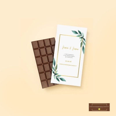 Barra de chocolate com rótulo branco decorado com folhas verdes e moldura dourada.