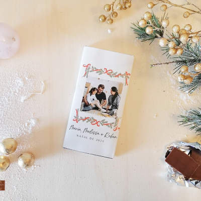 Embalagem de chocolate branca com foto e texto natalício, decorada com elementos dourados e pinheiro.