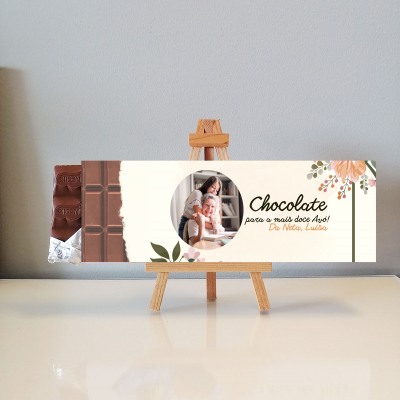 Embalagem de chocolate com texto dedicado e foto em cavalete de madeira sobre superfície branca
