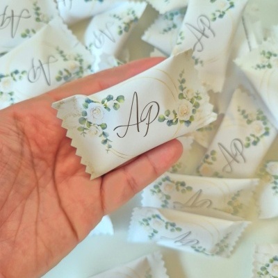 Pequenas embalagens brancas com padrão floral verde e branco e letras AP cinza, numa mão sobre várias embalagens semelhantes