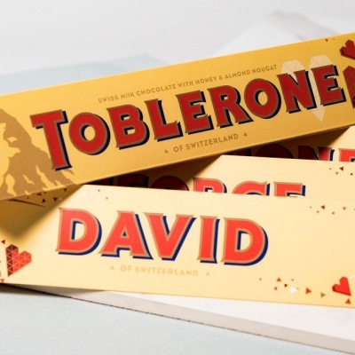 Caixas de Toblerone amarelas com personalização 'DAVID' e detalhes de corações e cartas.