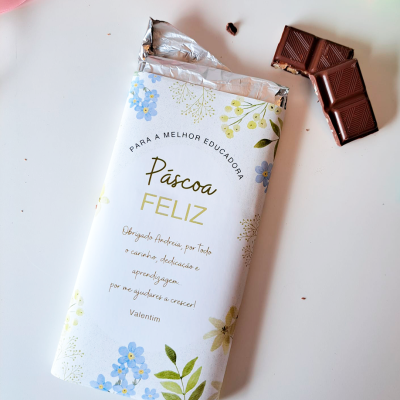 Barra de chocolate com embalagem floral e texto em português, com pedaços de chocolate ao lado.