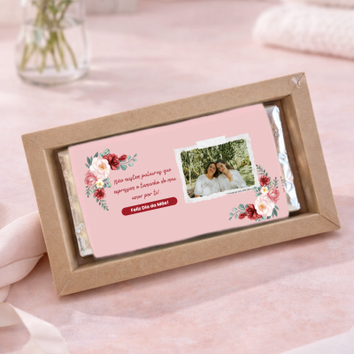 Barra de chocolate com rótulo rosa com flores e fotografia em embalagem de cartão castanho.