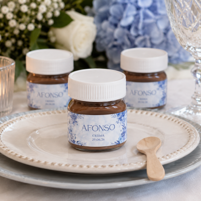 Frascos pequenos com creme castanho, etiqueta branca e azul com texto Afonso Crisma 29.06.26 em pratos com colher de madeira e decoração floral