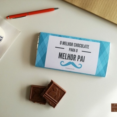 Barra de chocolate embrulhada com texto para o melhor pai, chocolate partido, caneta, caderno e chávena com bebida quente