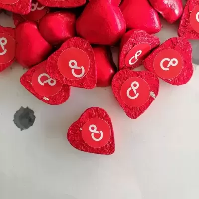 Chocolates em forma de coração embalados em papel vermelho com símbolos brancos sobre fundo branco