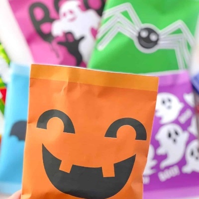 Pacote laranja com rosto de abóbora sorridente, outros pacotes de Halloween ao fundo