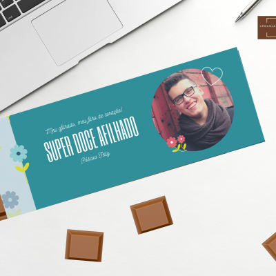 barra de chocolate com embalagem azul-turquesa, fotografia de homem e texto, pedaços de chocolate sobre mesa branca