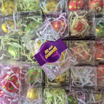 Caixas transparentes com ovos decorativos coloridos e etiqueta roxa com texto em português