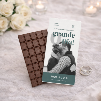 Barra de chocolate com cartão de convite e anéis em fundo claro com flores brancas