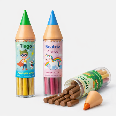 Embalagens cilíndricas transparentes com tampas em forma de pontas de lápis em azul, verde e laranja contendo palitos coloridos ou de chocolate e etiquetas personalizadas.