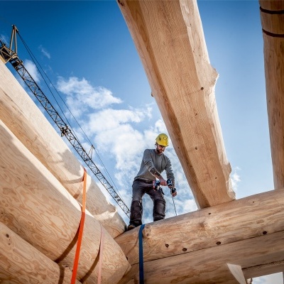 Homem com capacete numa estrutura de madeira sob céu azul.