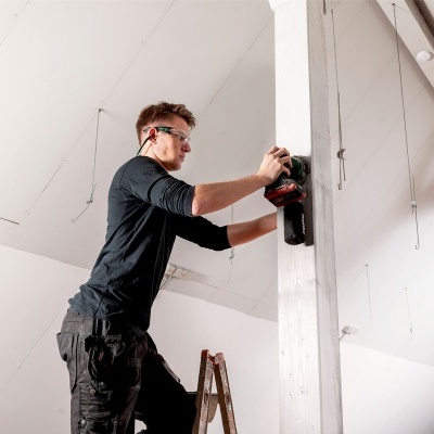 Homem a usar ferramenta elétrica numa viga branca num sótão