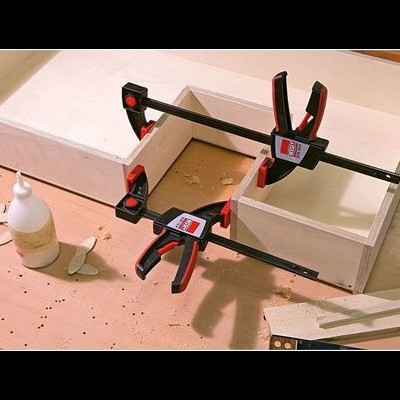 Prensas a fixar peças de madeira clara numa mesa de trabalho com cola e pedaços de madeira