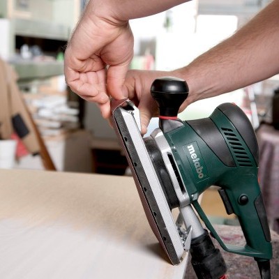Lixadora elétrica Metabo verde escura sendo ajustada por mão em oficina