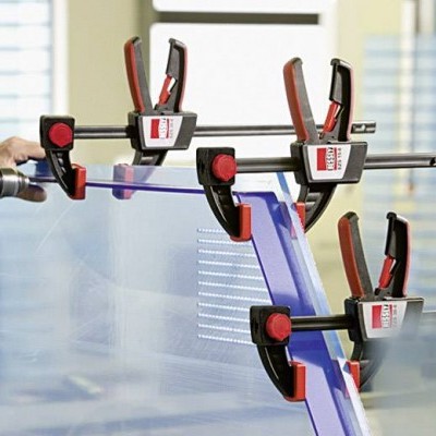 Pessoa a aparafusar placa transparente com furadeira e grampos vermelho e preto