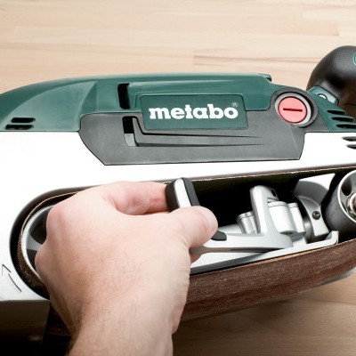 Aparelho de lixagem Metabo com mão a segurar sobre superfície de madeira