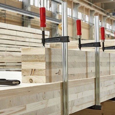 Painéis de madeira clara unidos por grampos metálicos com cabos vermelhos numa oficina.