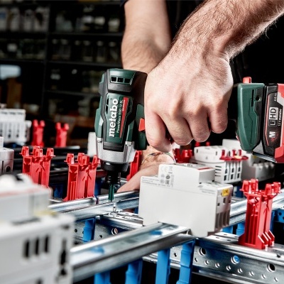 Parafusadora Metabo em uso numa estrutura metálica com componentes elétricos e suportes vermelhos