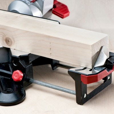 Serra de esquadria preta e vermelha com peça de madeira clara.