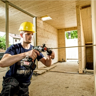 Homem com capacete amarelo a usar furadeira elétrica num interior de construção de madeira
