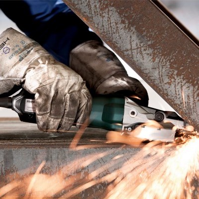 Trabalhador a cortar metal enferrujado com esmerilhadora elétrica gerando faíscas