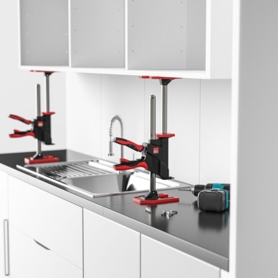Cozinha branca com bancada preta, grampos de aperto vermelhos e pretos, broca elétrica e parafusos na bancada