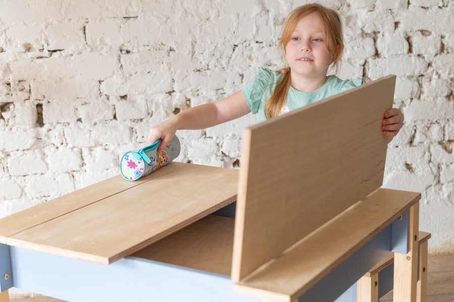 Conjunto de Mesa e Cadeira Infantil com Arrumação Garota usando um rolo limpa-pelos numa secretária de madeira clara