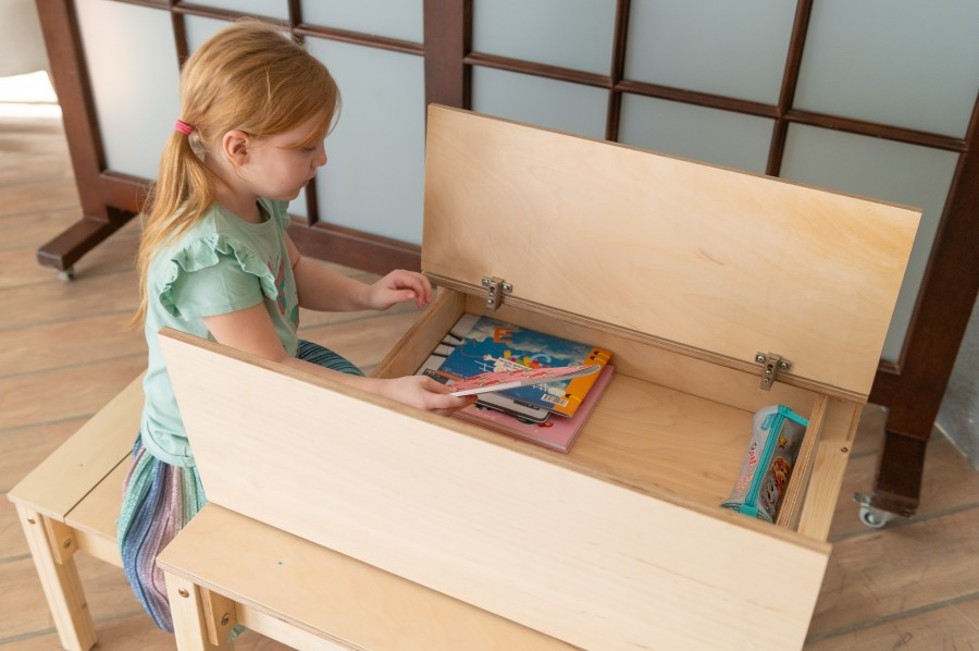Conjunto de Mesa e Cadeira Infantil com Arrumação Banco de madeira claro com compartimento aberto e criança a colocar livros dentro