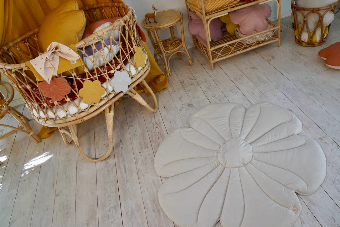 Tapete de Veludo FLOR Cadeira baloiço em rattan com almofadas amarelas e tapete branco em forma de flor num quarto com móveis em rattan.