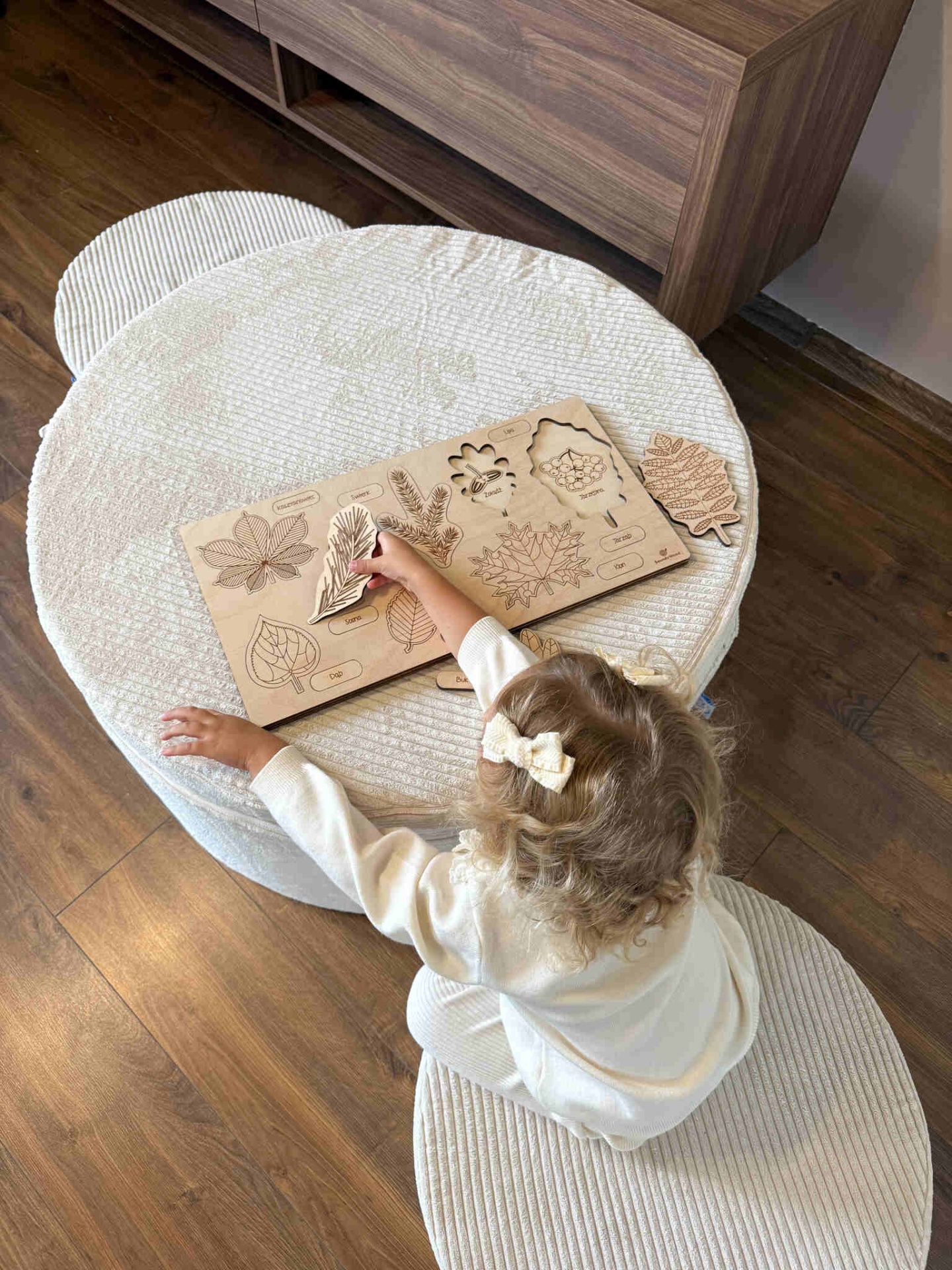 Conjunto Pufe Modular em Veludo Cotelê Bege Quebra-cabeças educativo de madeira com folhas e frutas, criança brinca em mesa branca texturizada.