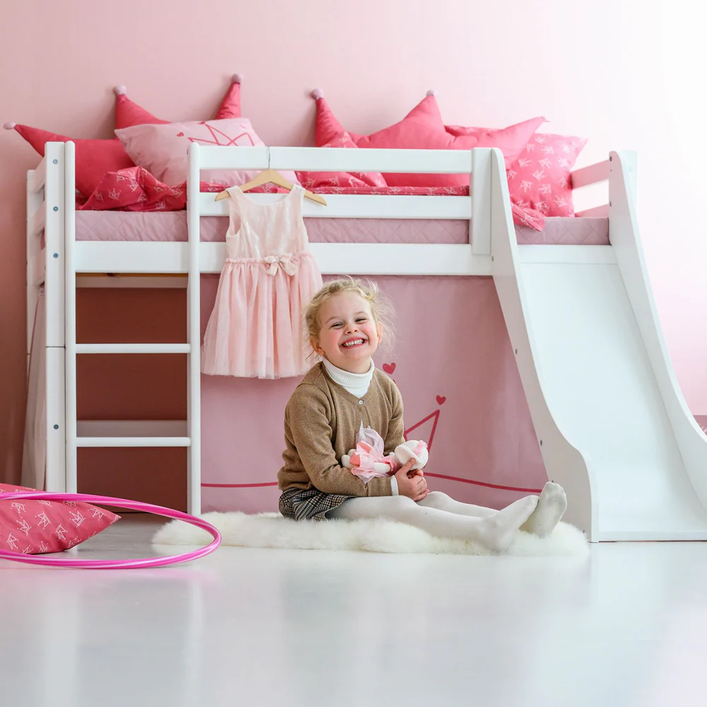 Almofadas Decoração Princesa Cama branca com escorrega e almofadas rosas, menina sentada no tapete branco.