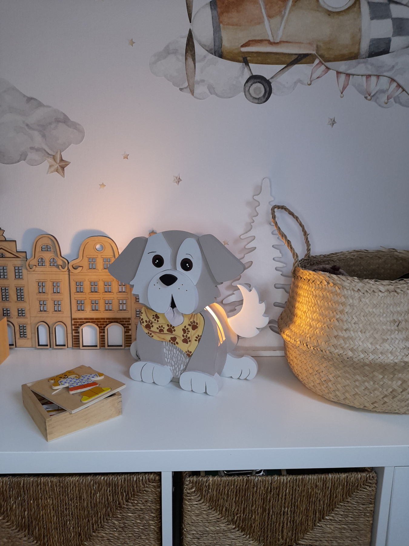 Candeeiro Cão de Madeira Controlado por SMARTPHONE Candeeiro de cão cinzento e branco com bandana, cesta de palha e decoração de madeira em bancada branca