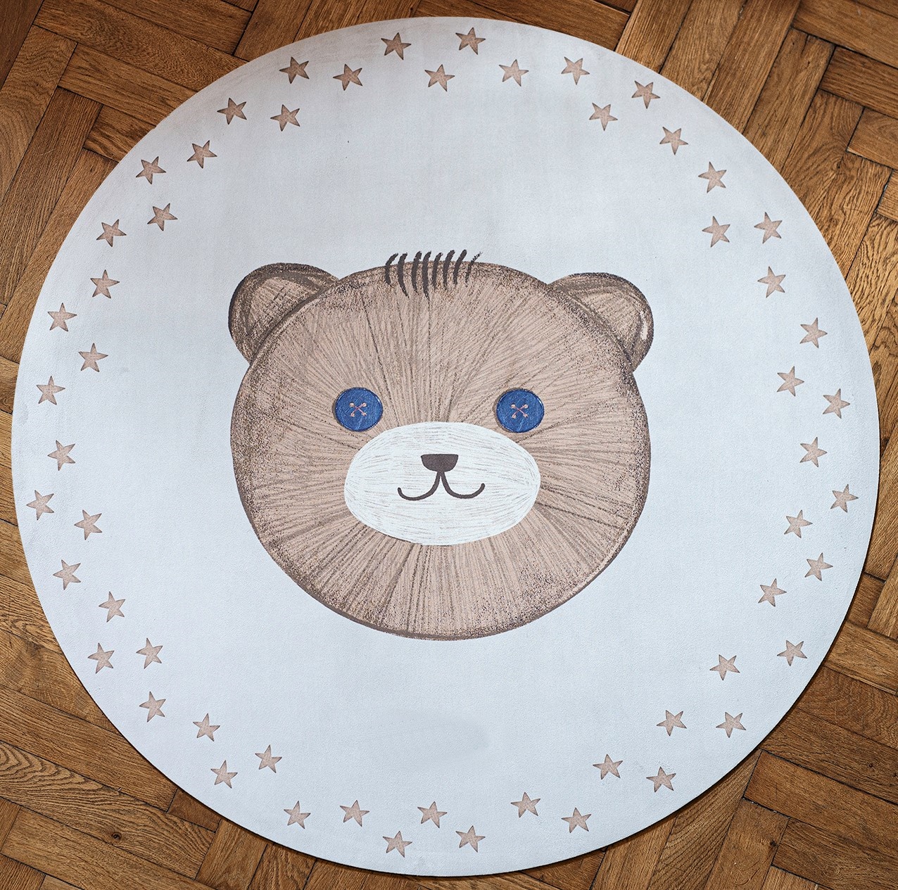 Tapete Redondo Borracha Natural URSO TEDDY Tapete redondo branco com desenho de urso ao centro e estrelas na borda sobre chão de madeira