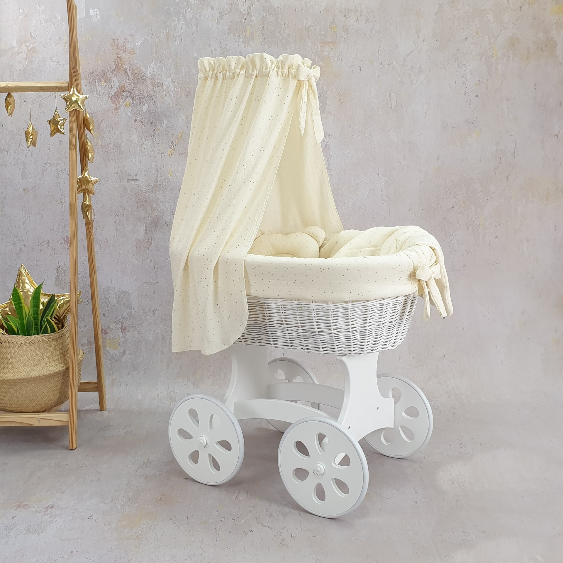 Cesta Moisés de Vime Branco SARA com Roupa de Cama Carrinho de bebé branco com cestinha de vime e dossel creme ao lado de suporte de madeira com estrelas e planta