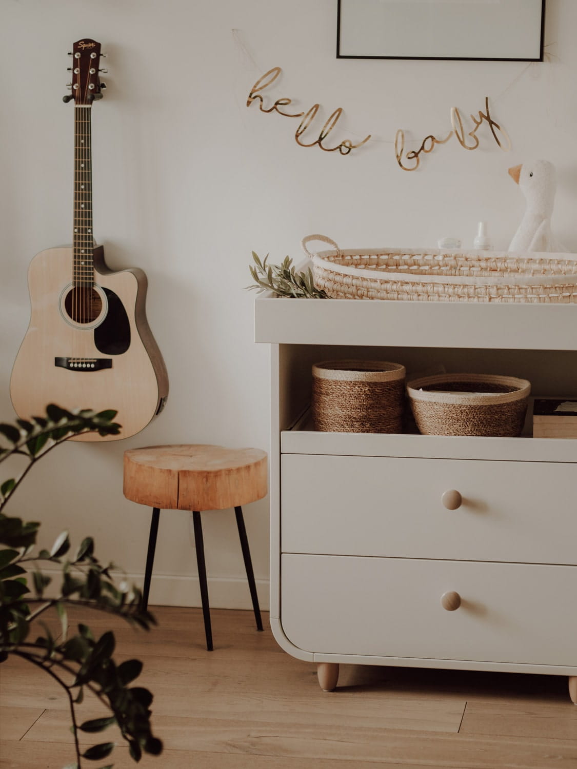 Cesto Fraldário de CASCA de MILHO Canto de quarto com guitarra, banco de madeira, cómoda branca e decoração 'hello baby'
