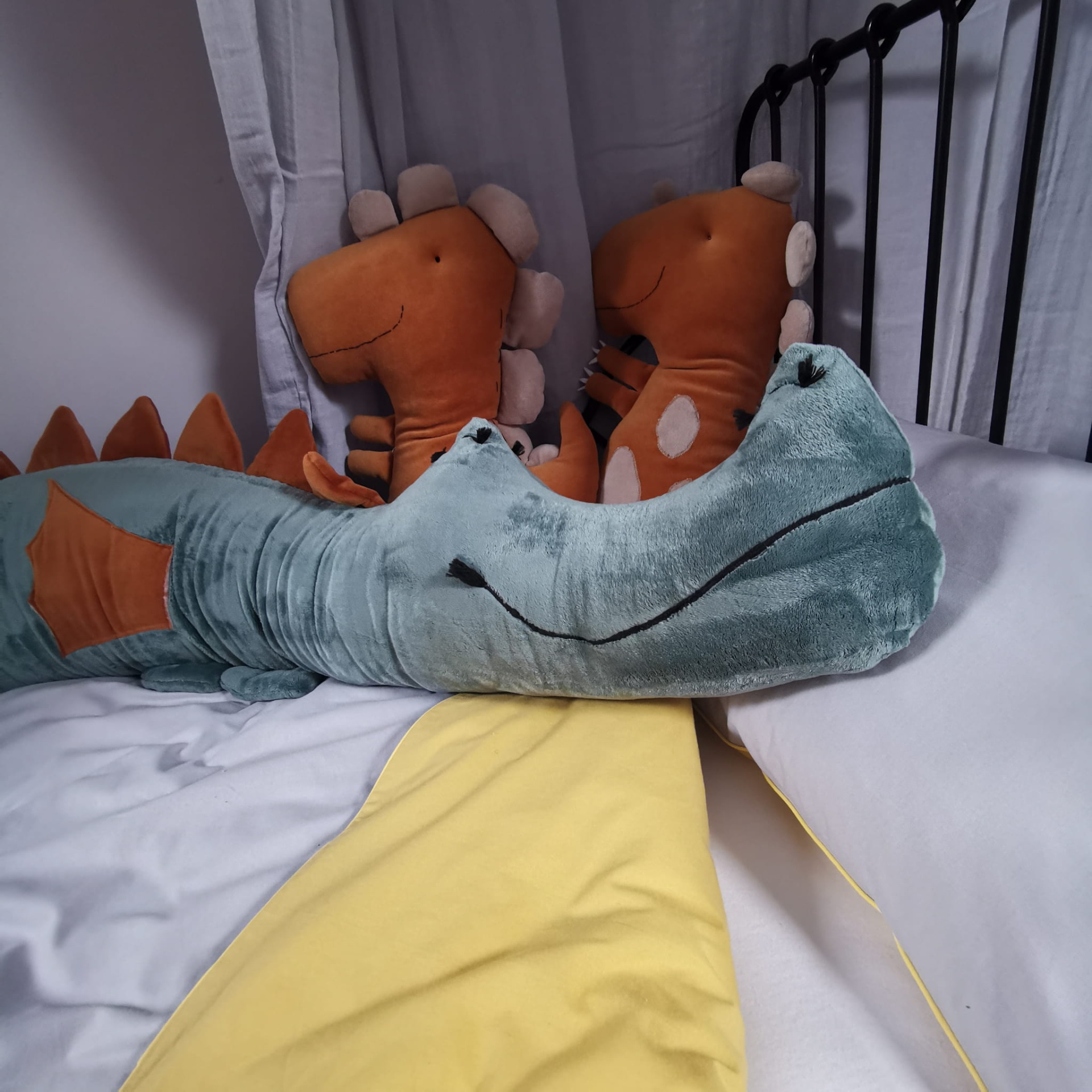 Protetor de Cama/Berço DRAGÃO PELÚCIA Almofadas de peluche dinossauro e crocodilo em cama com lençóis brancos e amarelos