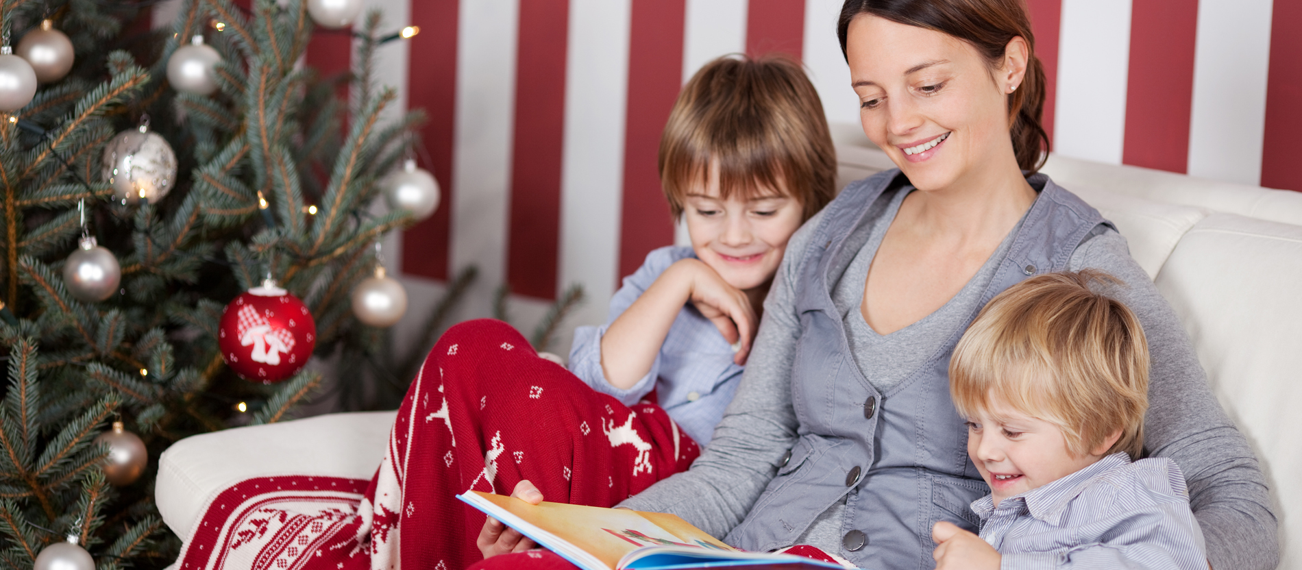 Mãe e duas crianças sentados no sofá com manta natalícia e árvore de Natal decorada
