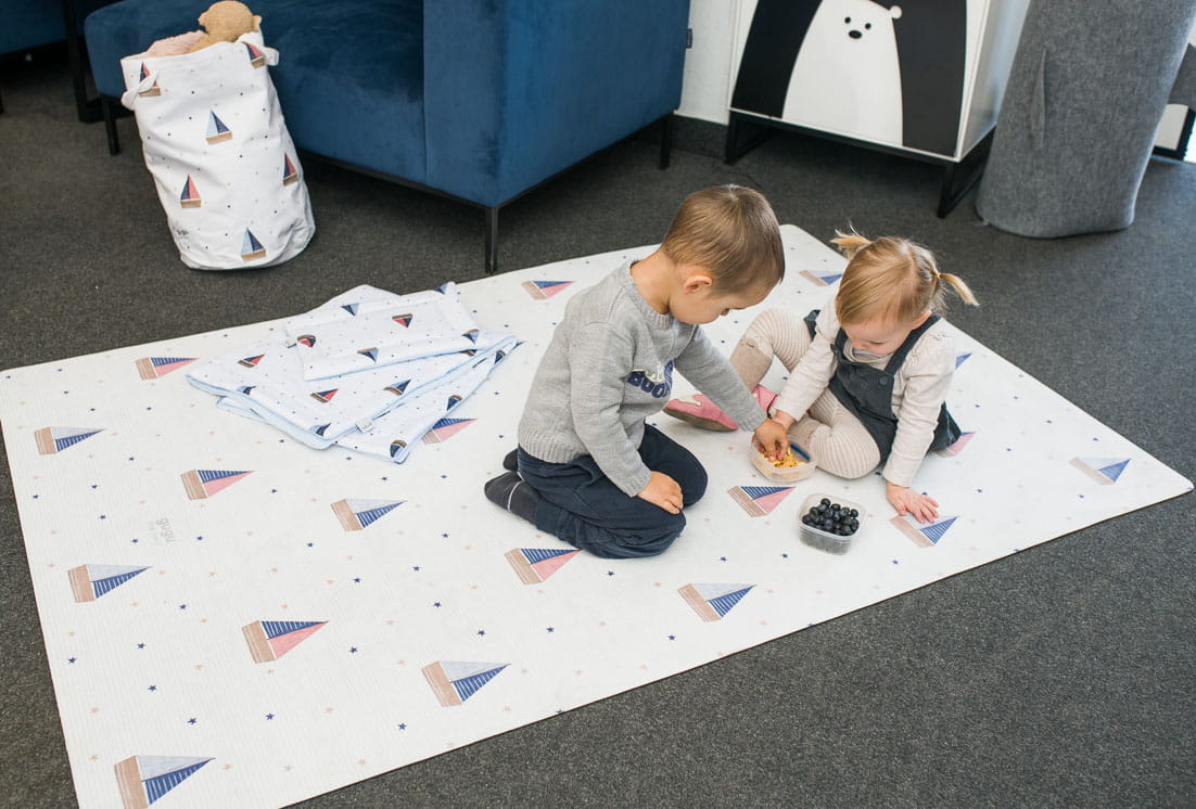 Tapete Ecológico PEQUENO MARINHEIRO Tapete infantil branco com veleiros coloridos e crianças a brincar.